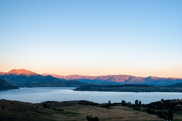 Fototapeta premium The sun sets over a mountain lake, casting a warm glow over the serene landscape and creating a peaceful, picturesque scene.