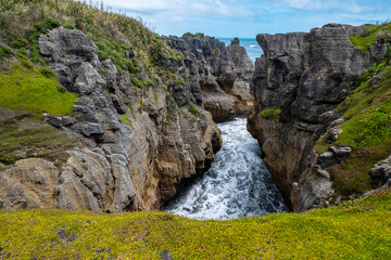 A scenic view of a rugged rock formation by the sea with lush green grass and plants growing on the cliffs under a partly cloudy sky.