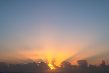 Obraz premium A beautiful sunset with the sun's rays streaming through clouds, casting a warm, golden light across the sky.