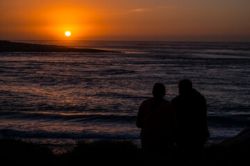 A beautiful sunset on the beach with silhouettes of people enjoying the view, the sky glowing with warm hues, and the ocean waves gently rolling.