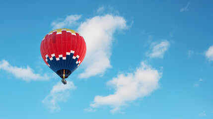 Hot air balloon in dark blue, red and yellow colors flying in a slightly cloudy blue sky