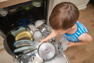 A young child is looking into a dishwasher full of dirty dishes. The boy is wearing a blue shirt...