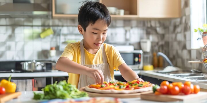 A young boy preparing a homemade pizza with fresh vegetables in the kitchen, promoting healthy eating.
