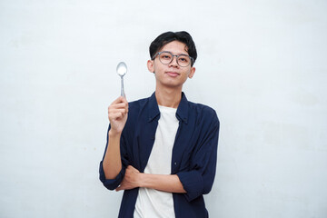 A portrait of happy Asian man wearing a blue shirt while thinking what to eat. Young man showing an pointing an empty mockup plate. Isolated with a white background.