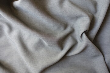 Surface of light gray polyester fabric with herringbone pattern in soft folds