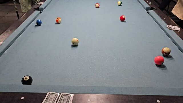 Close up of people playing 8-ball pool billiards at club. Pool is a classification of cue sports.