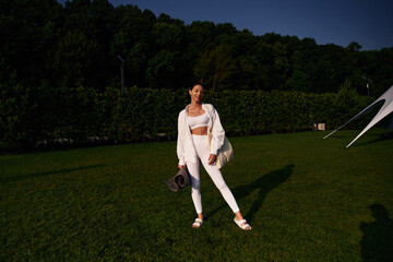 Happy smiling woman is standing on the green grass, trees at background