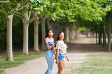 Fototapeta premium Two women walking in a park with trees in the background