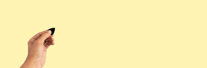 Male hand holding a guitar pick isolated on yellow background banner