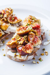 Breakfast toast with feta cheese, figs and pistachios on white plate, white background.