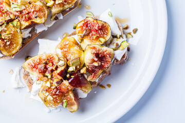 Breakfast toast with feta cheese, figs and pistachios on white plate, white background.