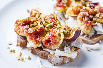 Breakfast toast with feta cheese, figs and pistachios on white plate, white background.