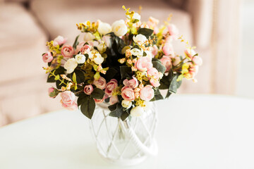 Elegant Floral Arrangement in Glass Vase on White Table. A beautiful floral arrangement in a glass vase with a white rope accent, placed on a white table.