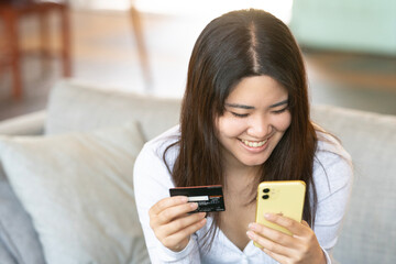 ソファに座ってスマホでカード決済をしている女性