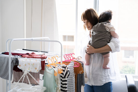 赤ちゃんを抱っこしながら洗濯を干している女性