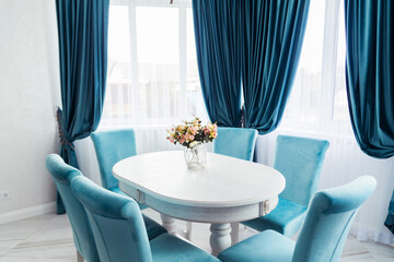 Elegant Dining Room with Blue Velvet Curtains and Chairs. Bright and elegant dining room featuring blue velvet curtains and chairs, a white table, and a floral centerpiece.
