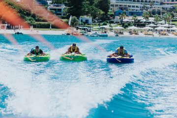 Three friends enjoying speedboat tubing on a sunny day near a beach resort