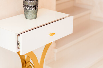 Close-up of a white console table with an open drawer and a decorative vase on top. The drawer...