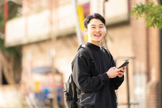 街でスマホを片手に笑っている男性