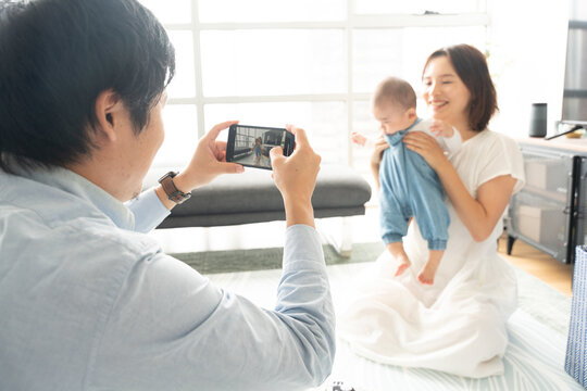 家で遊んでいる赤ちゃんと母親を撮影している父親