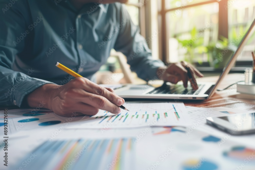 Poster business professional is focused on analyzing financial data using a laptop and documents in a moder