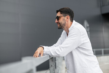 Handsome successful brutal business man in a fashion white shirt stands near a building in the city