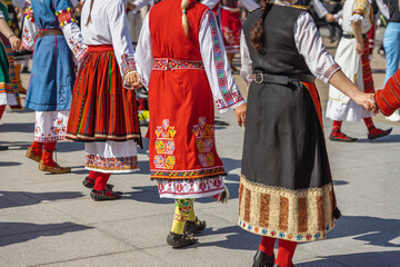 Women in bright colorful traditional Bulgarian costumes perform a horo round dance in city square