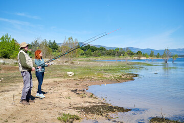 Fototapeta premium A man and a woman are fishing in a lake. They are holding fishing rods. The lake is calm and the sky is clear