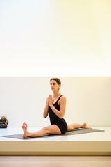 A woman is doing Hanumanasana or monkey yoga pose on a mat. She is in a split position and she is focused on her breathing.