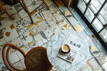 Top view of an empty table in a vintage European cafe. On the table are a cup of coffee and a newspaper
