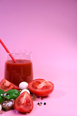 A glass of tomato juice with fresh tomatoes, mozzarella and basil on a pink background. Peppercorns and coarse salt on the surface. Healthy eating
