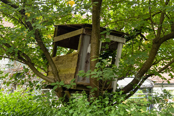 A rustic, homemade wooden treehouse built by children, nestled among lush green foliage.