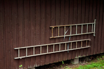 Metal ladders hanging on the dark brown old wooden wall of aged house in summer, holidays