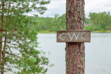 Wooden WC sign diy hanging on a tree in the forest with sea on a background, summer vacations in Finland