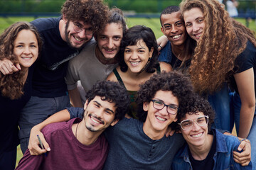 Obraz premium Life is brighter with friends. Portrait of a group of young students standing arms around each other outside in a park during the day.