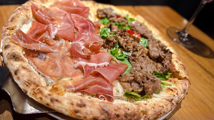In a pizzeria restaurant, a closeup of a delicious pizza with ham and beef meat