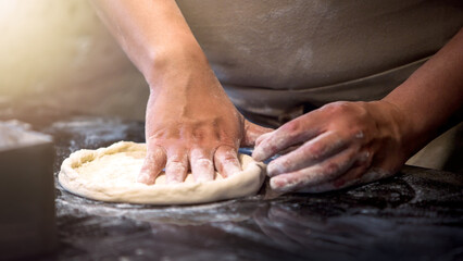 An Italian chef making pizza dough uses his hands to knead and roll it out.