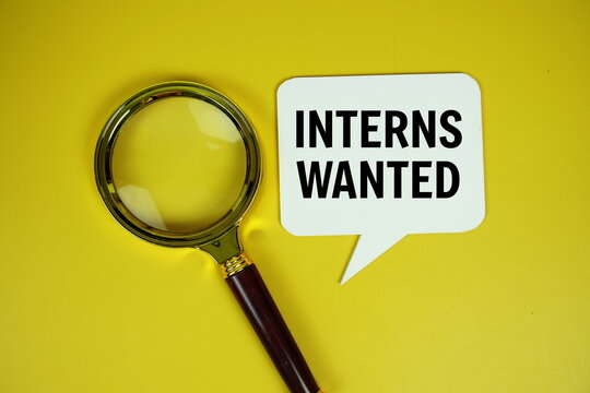 Interns Wanted text on speech bluble with magnifying glass top view on yellow background