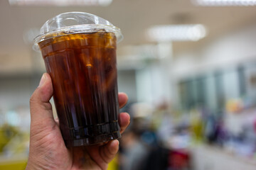 Someone hand holding a plastic cup of iced Americano in office