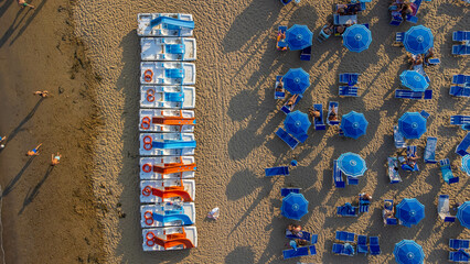 Top view of pedal boats along the beach with the sea. Aerial view of Mediterranean beach with sand and umbrellas. Colorful summer background expressing relaxation, summer vibes, sea, vacation, travel.