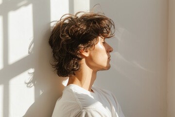 Fototapeta premium man facing the window side view, free-flowing hair with the breeze against the evening light and shadow on wall