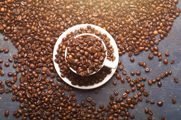 pile of roasted coffee beans, in the center cup with saucer full of beans, copy space