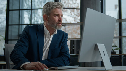 Mature focused thoughtful caucasian businessman marketing specialist working on computer in office man entrepreneur manager thinking analyzing finance digital data in Internet creating online project