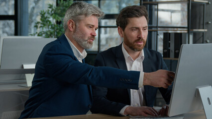 Mature businessman mentoring man discussing project on computer consulting investor client about digital investment in office Caucasian businessmen colleagues working together discuss data management