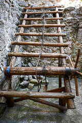 Old wooden medieval siege ladder with ropes and metal parts is leaning against a stone wall