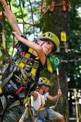 Obraz premium Two children wearing safety harnesses and helmets navigating a rope course in a park