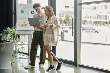 Two colleagues work together on a laptop, reviewing charts and graphs.