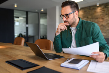 Focused young businessman auditing revenue report and planning budget while working at desk in...