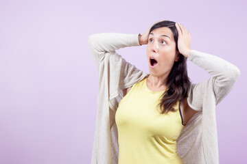 Naklejka premium Woman looks surprised to the side with hands on head isolated on lilac background. Concept of surprise and disbelief.