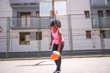 Naklejka premium African woman playing basketball under the sun in the city